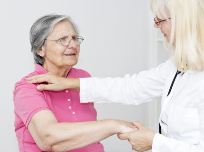 Female doctor looking at her female patient and touching senior women shoulder, giving  to her physical therapy.